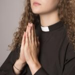 Photograph of a feminine person wearing a clerical collar and praying.