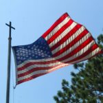 Photograph of an American flag flying from a flagpole with a cross at the top.