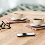 A photograph of cups of tea or coffee on saucers on a wooden table.