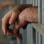 The Priest & the Prof Photograph of hands resting on prison cell bars.