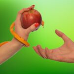Photograph of a feminine hand offering an apple to a masculine hand. The feminine hand has an orange snake wrapped around it with its head peeking out from behind the apple.