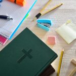 Photograph of a Bible on a table surrounded by school supplies.
